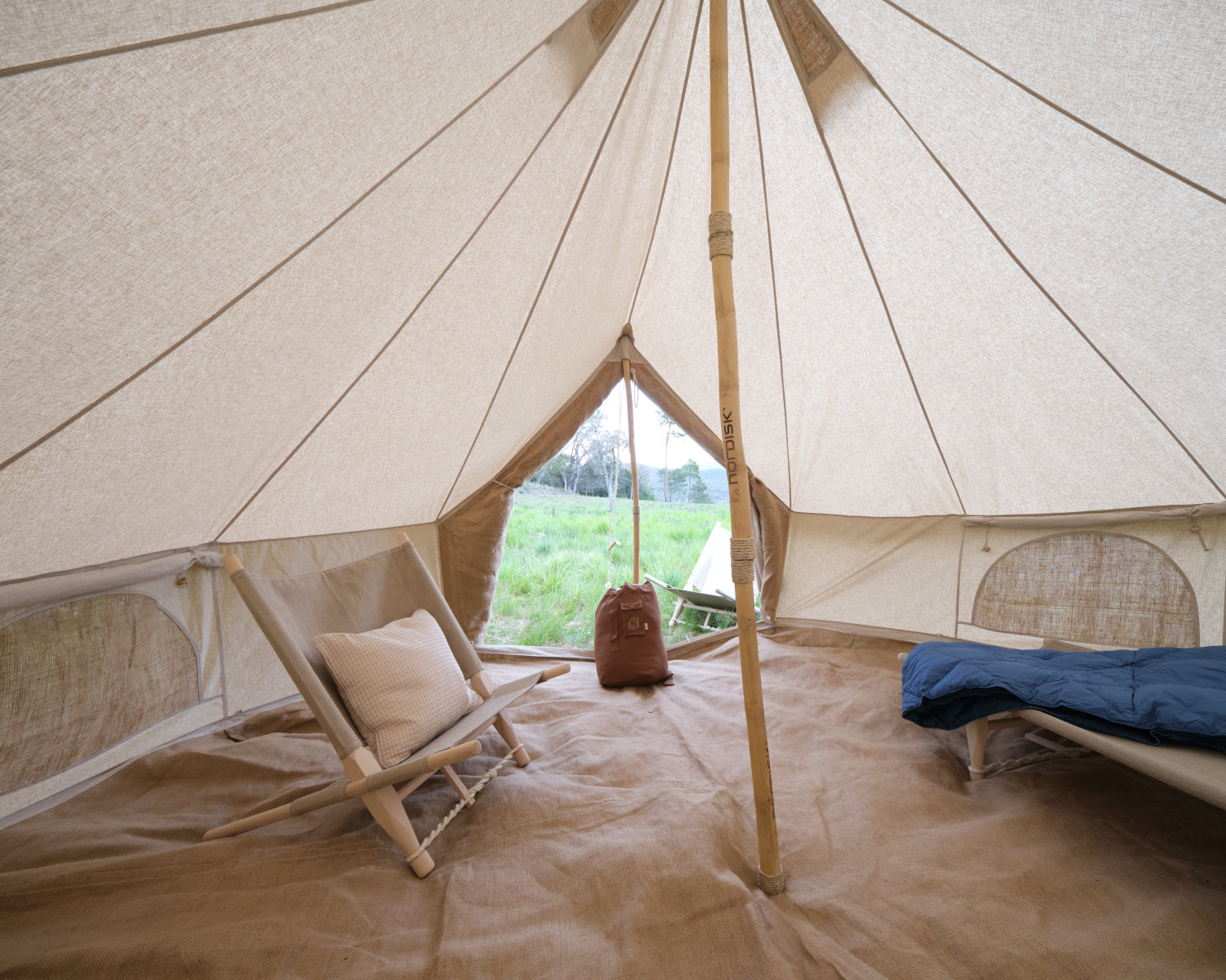Interior of a large beige tent with a wooden chair, pillow, and sleeping bag.