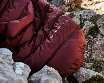 Close-up of a burgundy Nordisk down sleeping bag with Crystal Down insulation on rocky ground.
