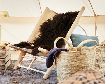 Wooden glamping chair with sheepskin and woven baskets inside a Nordisk technical cotton tent.