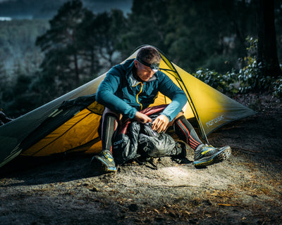 Hiker with headlamp sitting inside a Nordisk lightweight tent during a nighttime camping adventure.
