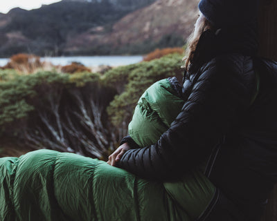 Person sitting in a green synthetic filling sleeping bag looking at a mountain landscape.