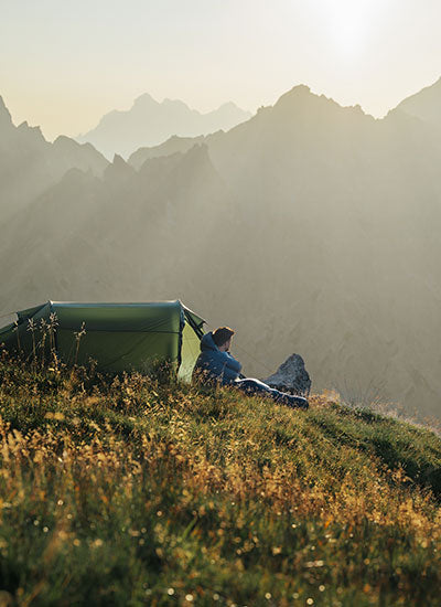 Man camping in a green Nordisk hiking tent overlooking misty mountains during sunrise.