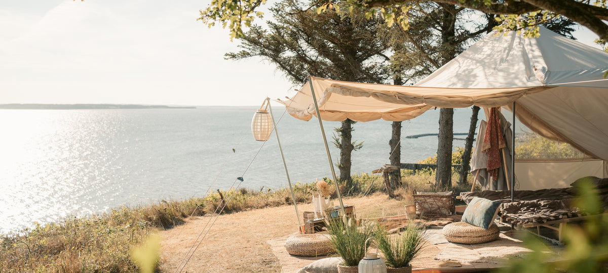 Luxury glamping setup with a Nordisk Utgard Sky tent overlooking the ocean at sunset.