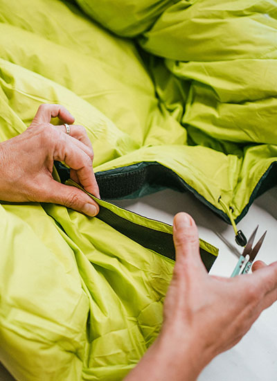 Hands repairing a green Nordisk sleeping bag as part of the Care and Repair programme.