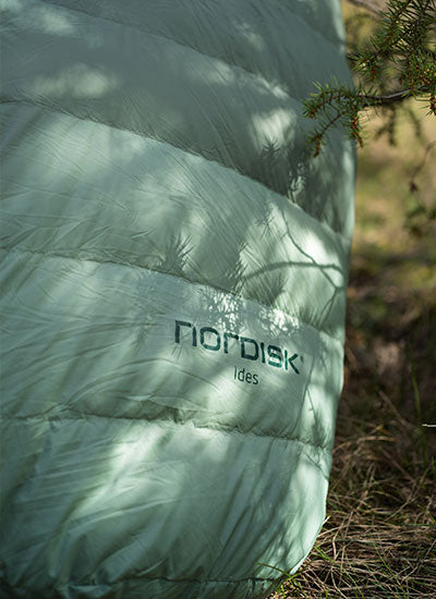 Close-up of a green Nordisk sleeping bag featuring the Care and Repair service logo outdoors.