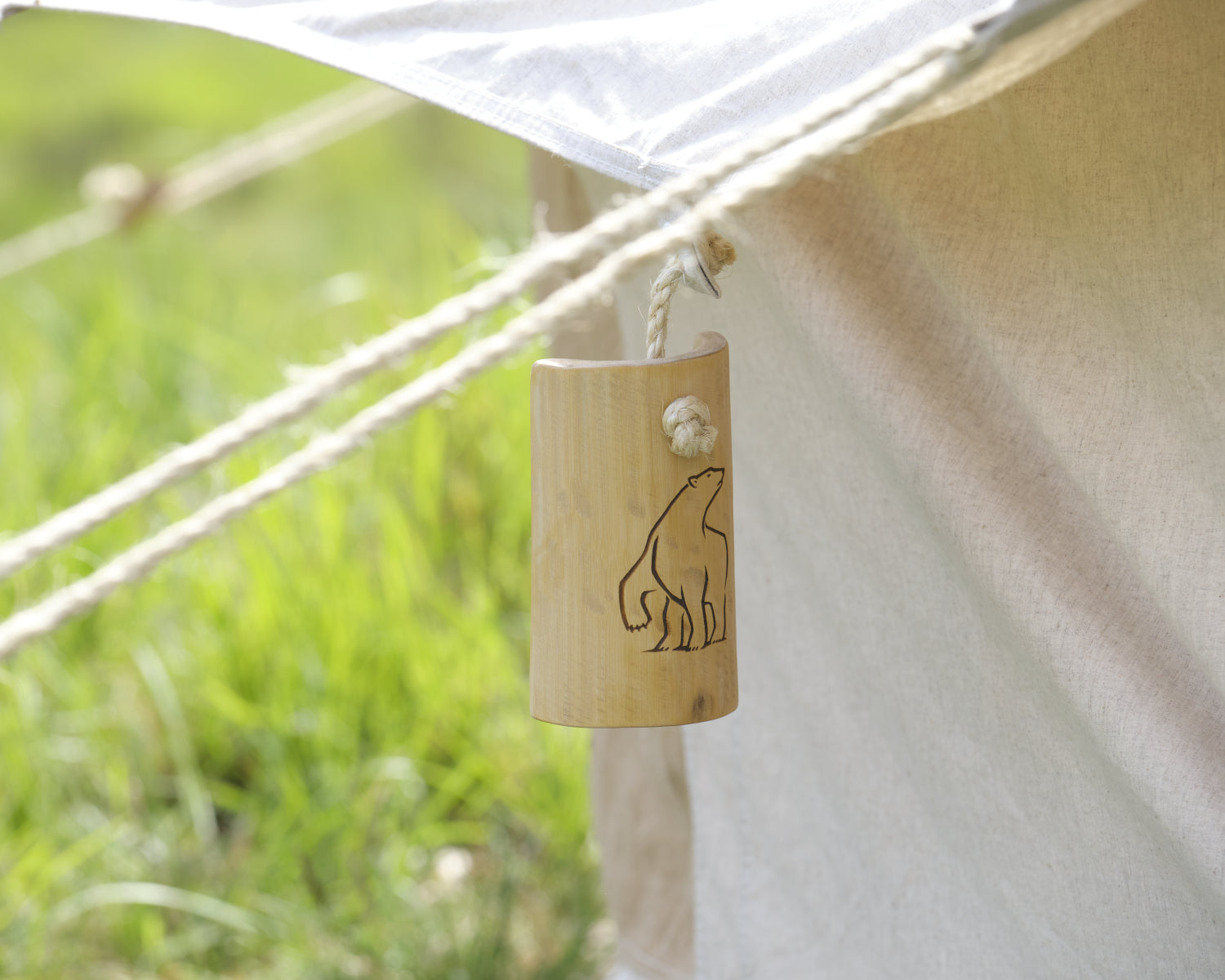 Wooden bell with bear design attached to a tent with grass in the background