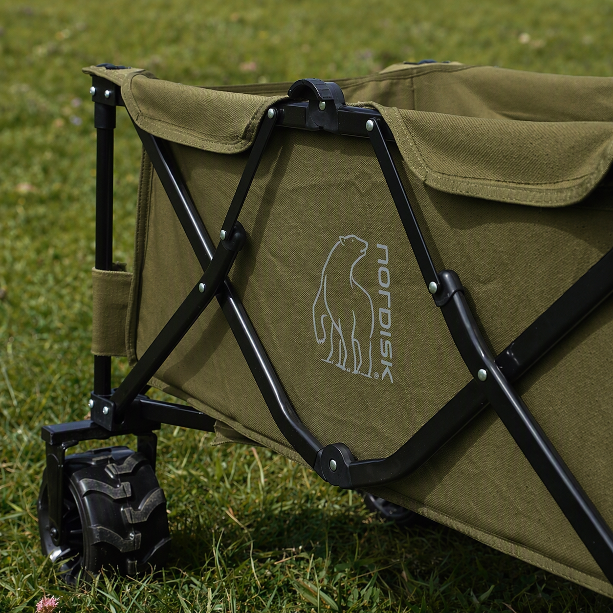 Green folding chair with black frame on grass, featuring a logo.